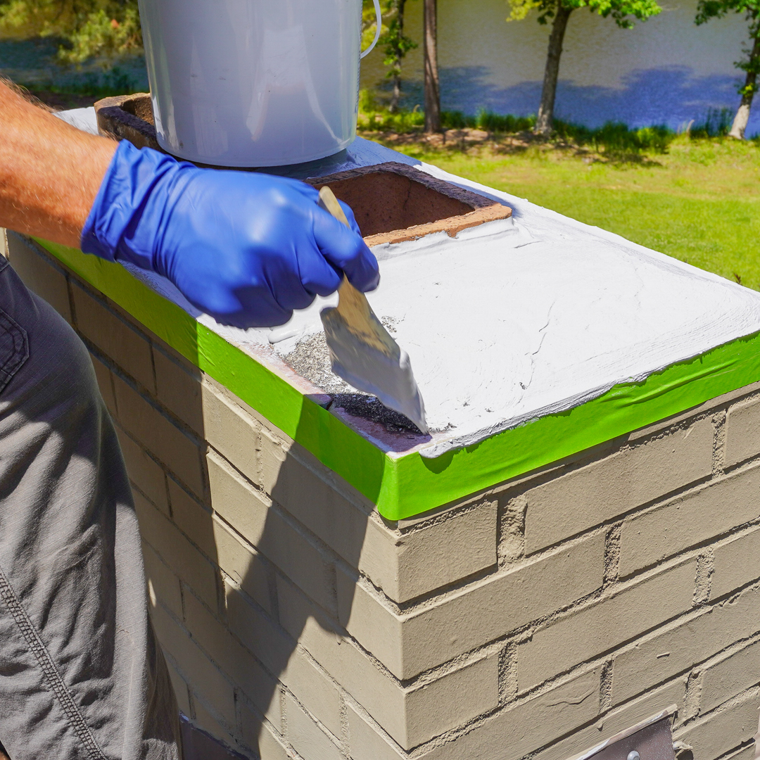 Person applying waterproofing compound to chimney crown, with a focus on preventing water damage in Florida.