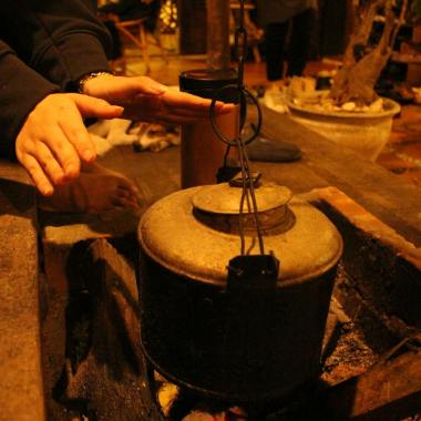 Close-up of hands warming near a rustic pot by the fireplace, creating a cozy atmosphere.